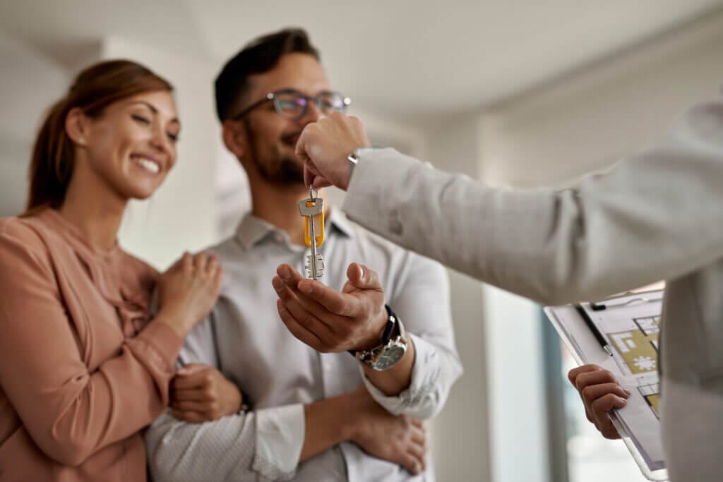 Real estate agent handing keys to a couple, symbolizing a non contingency offer.