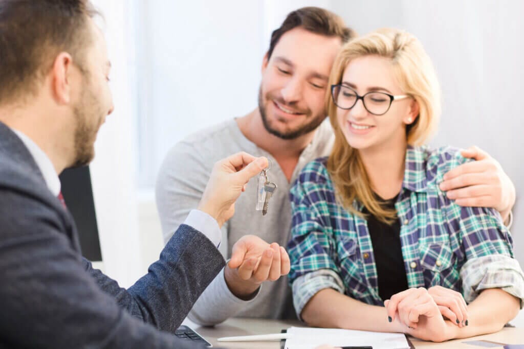 Sales manager handing keys to a young couple, representing key housing finance solutions.