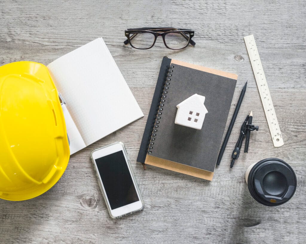 Notebook, pen, and builder helmet on a desk, representing construction loan contingent on home sale.